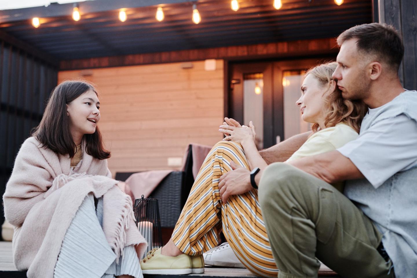 Parents et adolescente assis sur une terrasse le soir, en pleine conversation