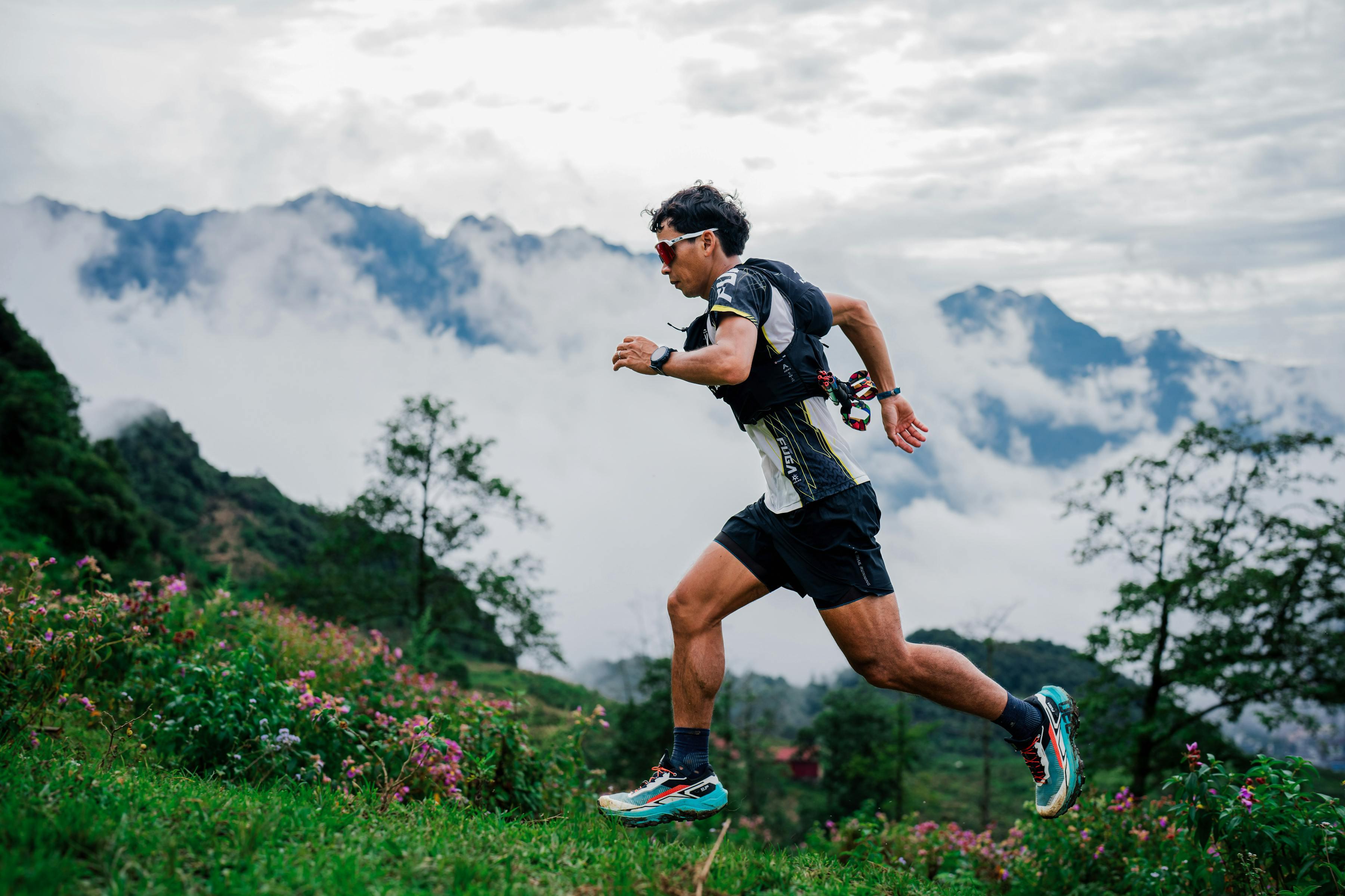 Coureur en pleine course avec montre GPS sur un sentier de trail en montagne